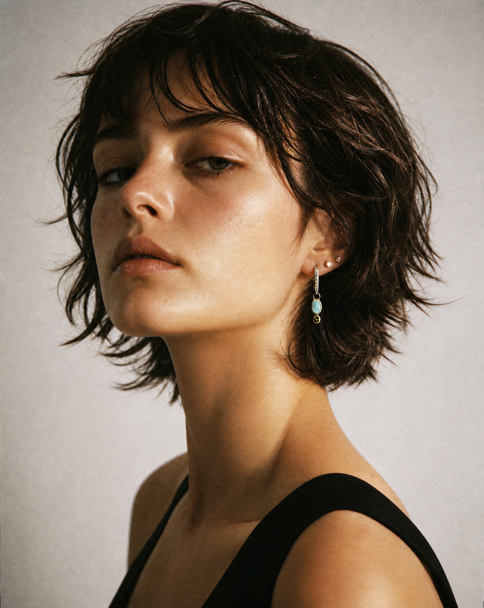 Woman with short dark hair wearing earrings against a neutral background