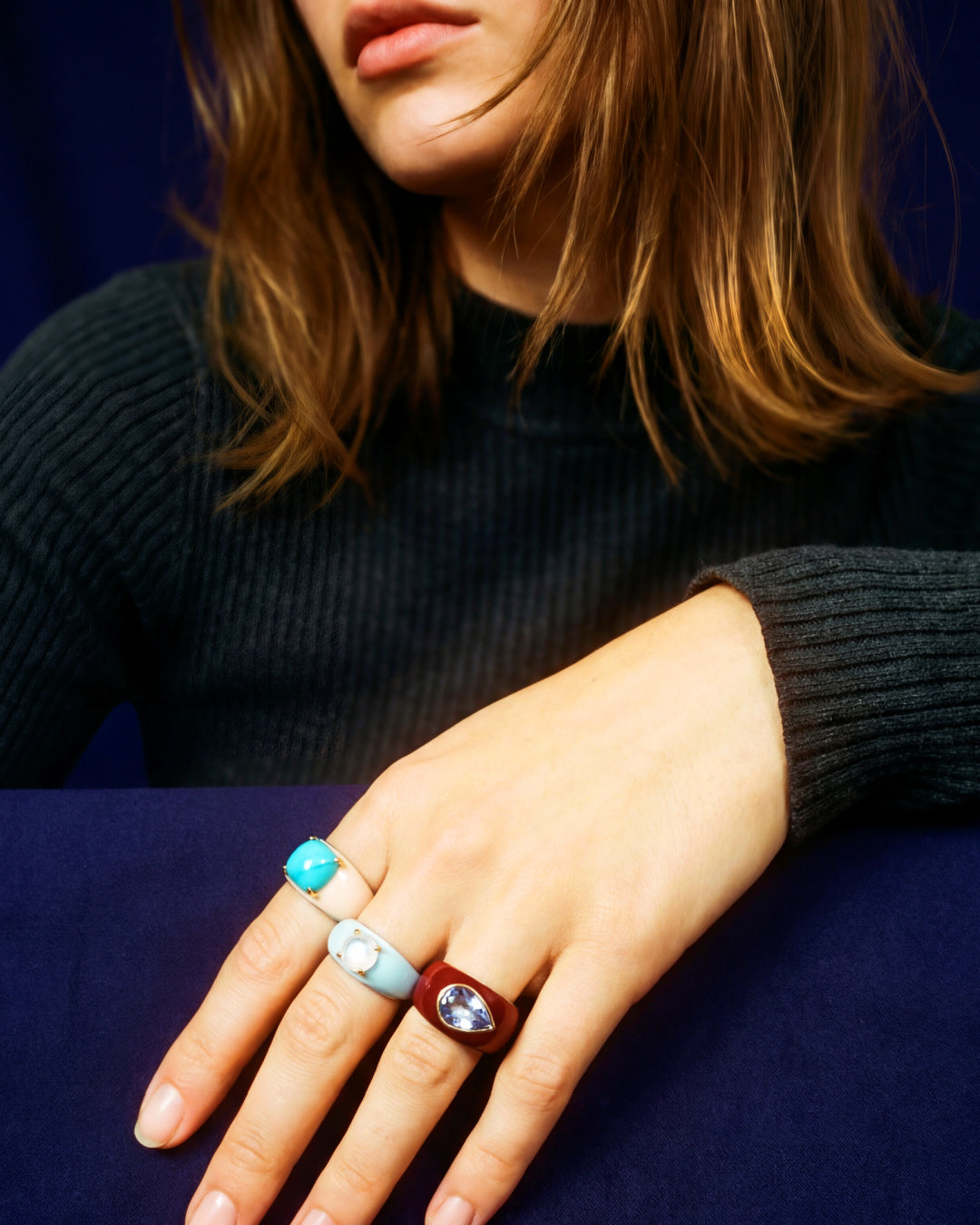 Close-up of a person's hand wearing three rings with turquoise, silver, and brown bands on a dark background.