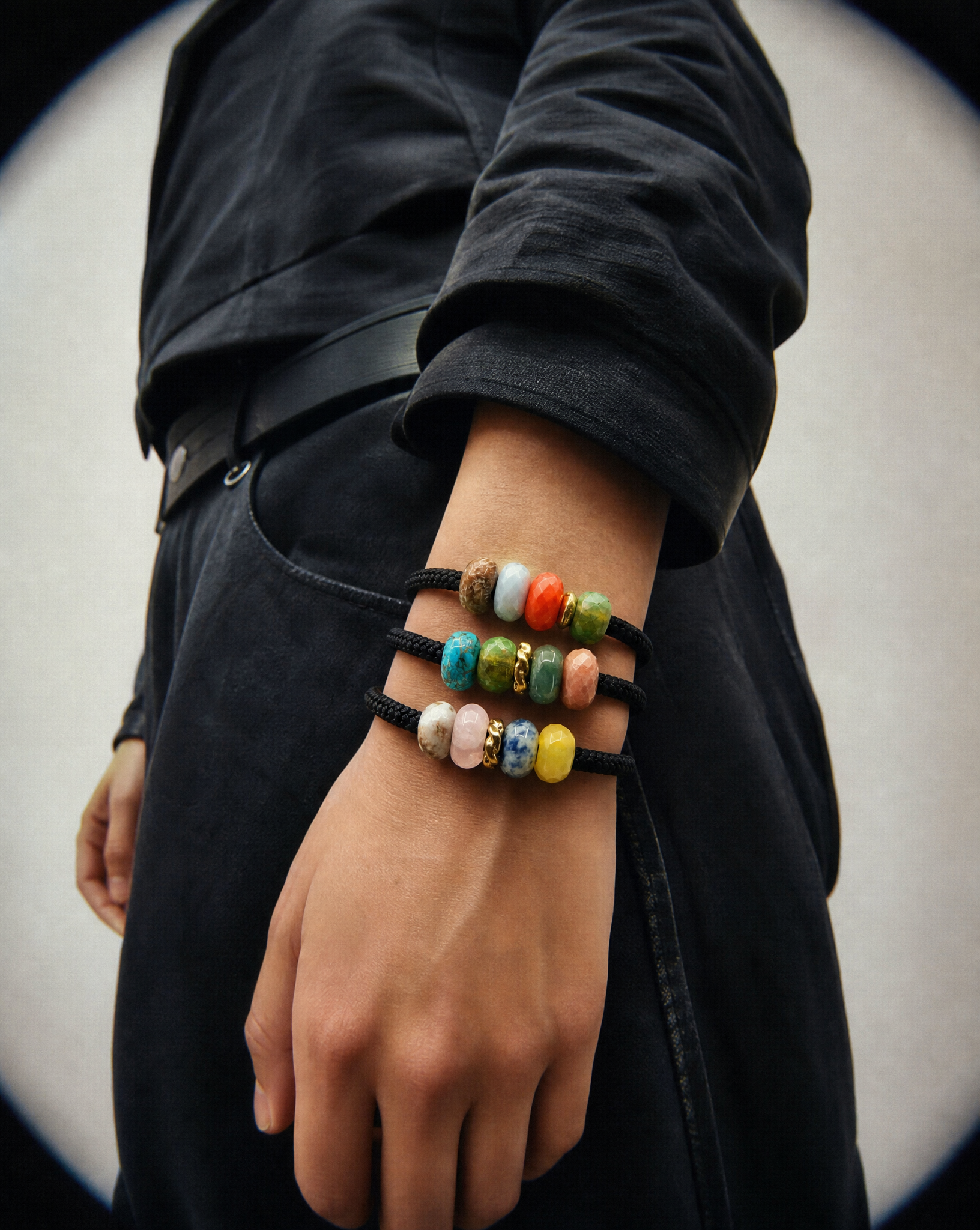A close-up of a person's wrist wearing three stacked black cord bracelets adorned with colorful, marbled stone-like beads in shades of blue, green, orange, pink, yellow, and white.